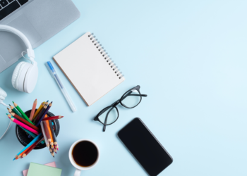 Un carnet, des crayons et des lunettes posées sur une table bleue