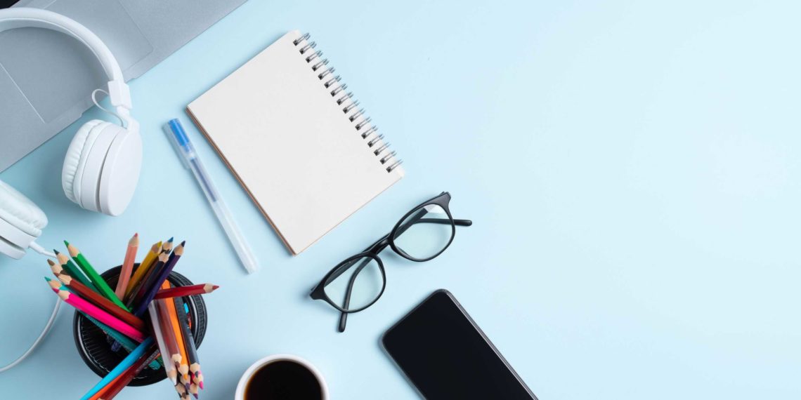 A notebook, pencils and glasses on a blue table