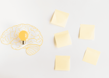 5 Post-it jaunes sur une table avec à gauche un dessin d'un cerveau jaune avec une ampoule au centre jaune aussi