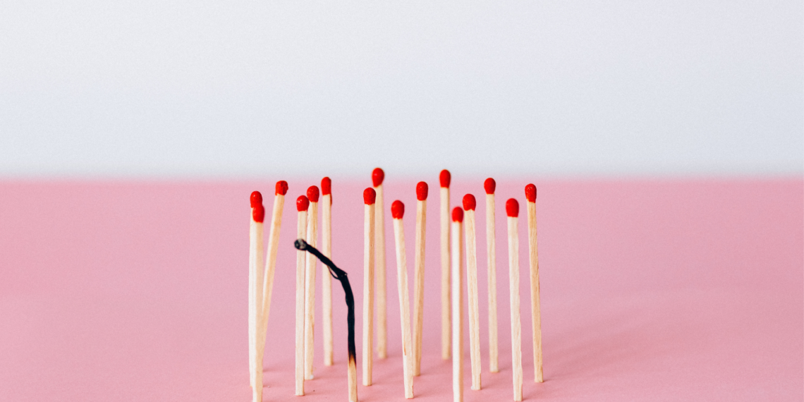 un jeu d'allumettes sur fond rose et blanc, l'une d'entre elles étant brûlée pour représenter le travail qui brûle un individu de l'intérieur
