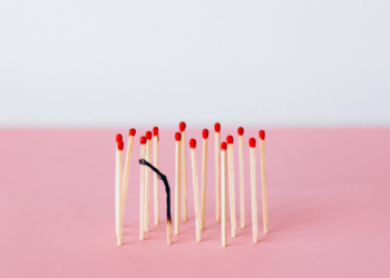 un jeu d'allumettes sur fond rose et blanc, l'une d'entre elles étant brûlée pour représenter le travail qui brûle un individu de l'intérieur