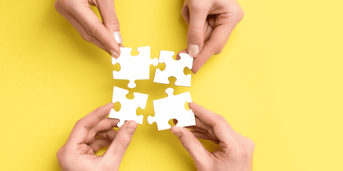 4 hands on a yellow background reaching for the puzzle pieces
