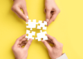 4 hands on a yellow background reaching for the puzzle pieces