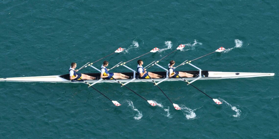 A team of 4 rowers rowing together on a blue lagoon