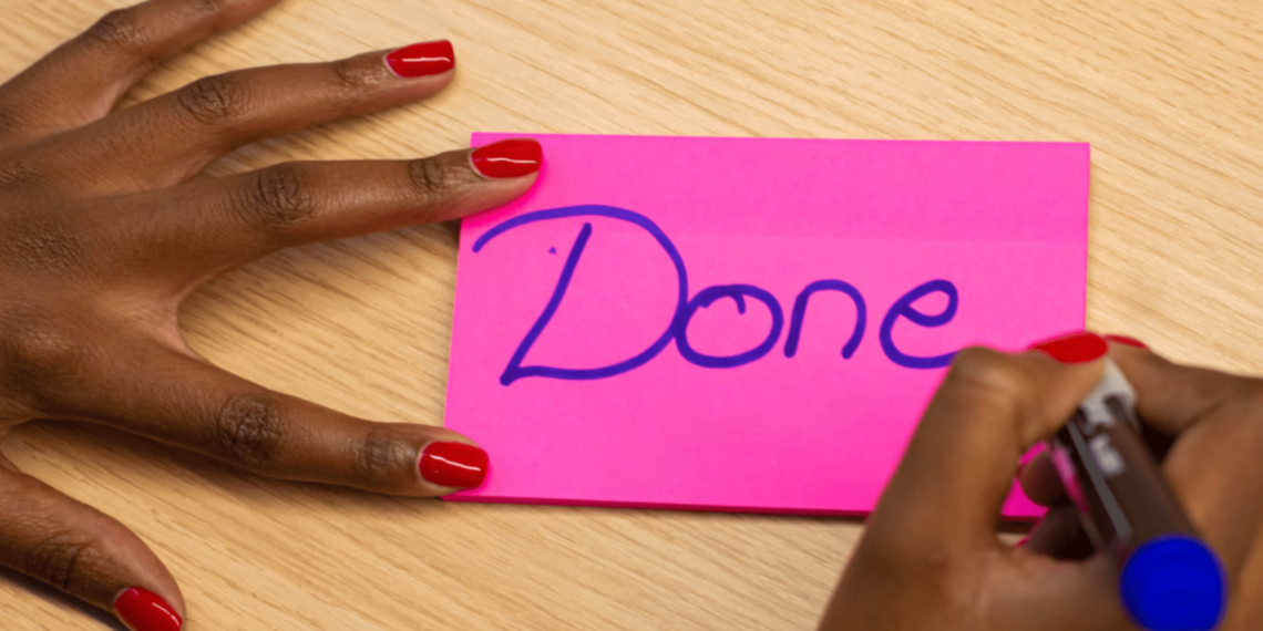 Pink Post-it on which a woman writes Done with a pen