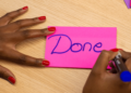Pink Post-it on which a woman writes Done with a pen