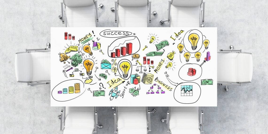 A white meeting table with graphics and data on top of it. 8 chairs around the table on a concrete floor.