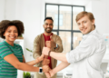 Trois membres de l'équipe participent activement à un jeu collectif. Ils sont disposés en cercle dans un espace ouvert et dégagé, souriants et concentrés.