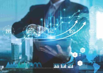 Personne en costume qui tient une tablette numérique. Des chiffres et graphiques d'un bleu néon ressortent de l'écran